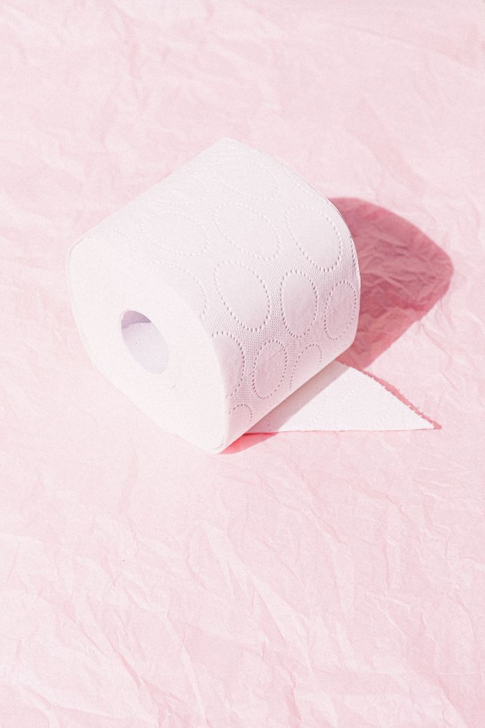 Home A toilet paper roll on crinkled pink paper with bright lighting.